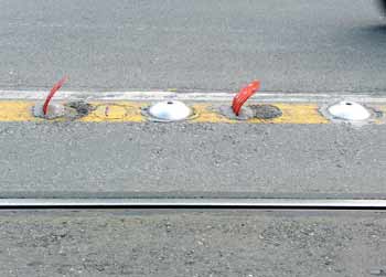 Large road studs which have been embedded into the road surface and alternate with red plastic flaps.