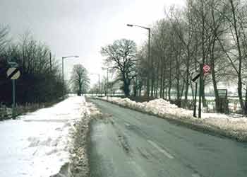 A single carriageway road with deep snow partially narrowing it so that only the road center is clear.