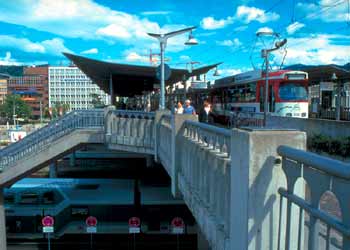 Light rail stop on traffic-free bridge at railway station.