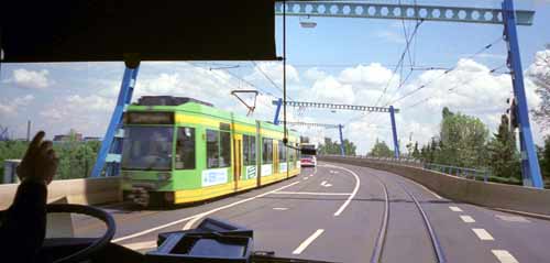 View out buses' front window, see tram approaching in other direction.