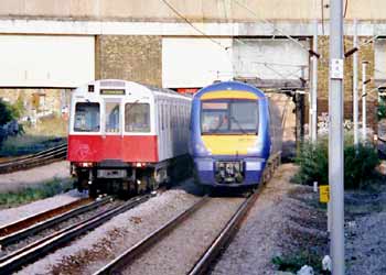 District line Underground train and class 357 mainline train side by side on shared route in East London.